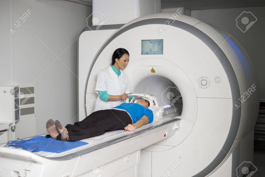 Female doctor fixing face mask to patient lying on MRI scan machine in hospital